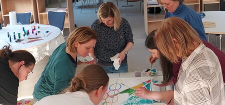 Frauen stehen um einen Tisch und malen