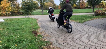 Auf einen Weg fährt ein Motorrad vor einem Lastenfahrrad.