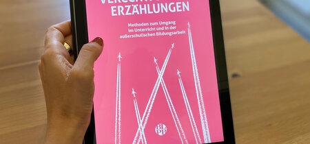 Verschwörungserzählungen. Das Buchcover ist im Tablet zu sehen. 
