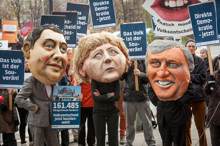 Darsteller mit Großmasken von Gabriel, Seehofer und Merkel