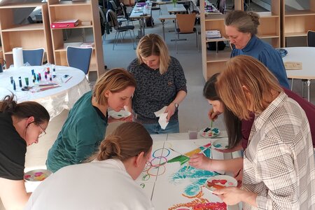 Frauen stehen um einen Tisch und malen