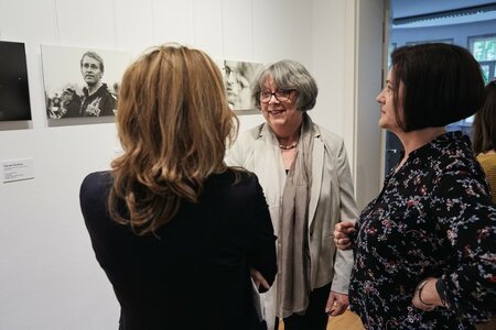 Martina Schellhorn (Mitte), ehemalige Mitarbeiterin der Landeszentrale und dort zuständig für Ausstellungen, im Gespräch mit Janin Hinze, in der Landeszentrale zuständig für Förderung - im Hintergrund eine Fotografie von Daniel Günther (CDU), Ministerpräsident Schleswig-Holstein.