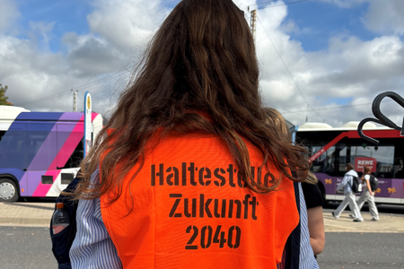 Eine junge Frau trägt eine orangene Weste mit der Aufschrift "Haltestelle Zukunft"