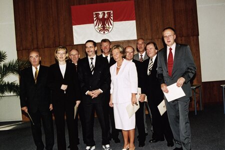 Das Brandenburger Kabinett vor der Brandenburger Landesfahne - die Minister halten ihre Ernennungsurkunden in Händen. Foto: LISUM