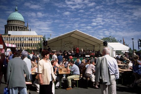 Festbühne mit Kapelle auf dem 3. Brandenburger Gartentag links im Hintergrund ist die Kuppel der Nikolaikirche und die Fachhochschule Potsdam zu sehen im Vordergrund stehen Passanten vor der Bühne sitzen Leute auf Bänken an Tischen und essen und trinken