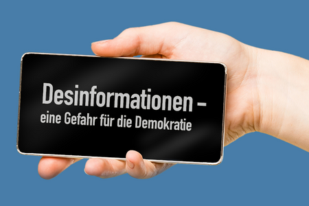 Eine Hand hält ein Smartphne. Darauf steht: "Desinformationen - eine Gefahr für unsere Gesellschaft".