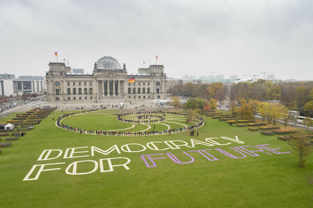 Die Demokratie der Zukunft wird von und mit uns allen gestaltet. Eine große Spirale vor dem Reichstag – geformt aus goldglänzendem Stoff und Hunderten von Menschen – greift die Form der Reichstagskuppel auf. Sie bildet eine Brücke von den Menschen auf der Wiese zu den Menschen im Bundestag. Das Motto: "Democracy for Future."