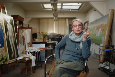 Doris Ziegler im Künstleratelier sitzend, in die Kamera schauend.
