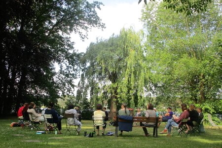 Seminar-Gruppe in der Villa Fohrde: Teilnehmende sitzen im Stuhlkreis auf einer Gartenwiese unter einer großen Trauerweide. Im Hintergrund ist die Havel sichtbar. Hier wird Demokratie nicht nur besprochen, sondern im Miteinander erlebt.