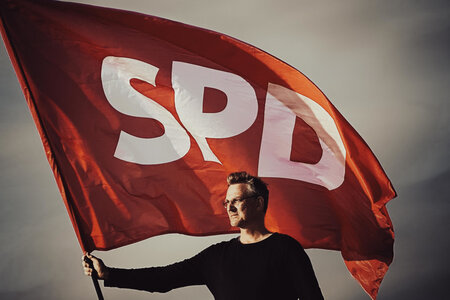 Filmplakat "Unten im Ortsverein". Ein Mann hält eine SPD-Fahne