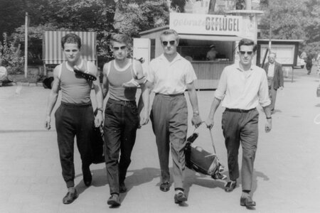 Im Vordergrund des Fotos stehen vier junge Männer. Im Hintergrund sieht man ein Imbisstand. 