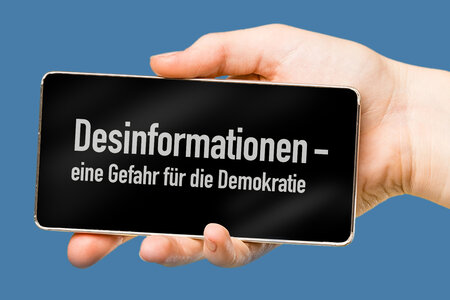 Handy mit der Aufschrift Desinformationen - eine Gefahr für die Demokratie