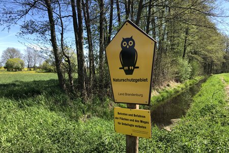 Foto mit einem gelben Schild für Naturschutz mit einer schwarzen Eule darauf