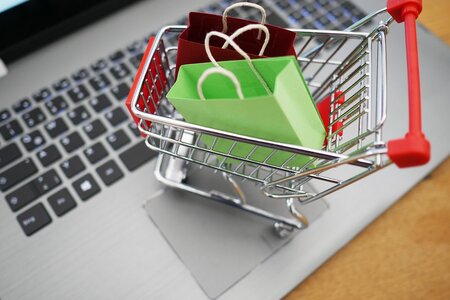 Ein Einkaufswagen mit Tüten auf einer Tastatur vor dem PC