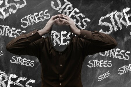 Kopfloser Mann vor einer Tafel, auf der mehrmals das Wort Stress geschrieben steht