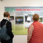 Leute stehen im Veranstaltungsraum der Landeszentrale und sehen sich die Ausstellung "Stadt, Land, Klima. Klimawandel und Nachhaltigkeit in Brandenburg" an.