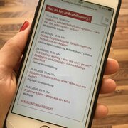 Eine Hand hält ein Smartphone. Das Display zeigt den Veranstaltungskalender der Landeszentrale