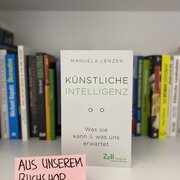 Im Hintergrund eine Reihe Bücher. Im Vordergrund das Buch "Künstliche Intelligenz. Was sie kann & was uns erwartet" von Manuela Lenzen. 