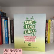 Im Hintergrund eine Reihe Bücher. Im Vordergrund das Buch "Stadt, Land, Klima. Klimawandel und Nachhaltigkeit in Brandenburg".