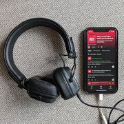 Ein Smartphone. Auf dem Display ist der Spotify-Kanal der Landeszentrale zu sehen. Neben dem Smartphone liegen Kopfhörer. 