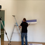 Ein Mann steht mir einer großen Rolle in der Hand an einer Leiter.