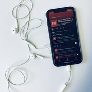 Ein Smartphone mit Kopfhörern. Auf dem Display des Smartsphones ist der Podcast "Was ist da los? Über Politik und Gesellschaft" der Landeszentrale zu sehen. 