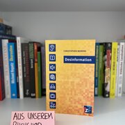 Im Hintegrund eine Reihe Bücher. Im Vordergrund das Buch "Desinformation" von Christopher Nehring.