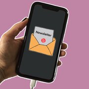 Eine Hand hält auf ein Smartphone. Auf dem Display sieht man einen geöffneten Briefumschlag. Aus dem Briefumschlag guckt ein Briefbogen. Darauf steht das Wort "Newsletter", darunter befindet sich das Logo der Landeszentrale.