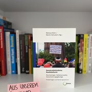 Im Hintergrund eine Reihe Bücher. Im Vordergrund das Buch "Demokratiefeindliche Realitätsflucht: Reichsbürger, Selbstverwalter, Verschwörungsgläubige" von Markus Klein und Martin Schubert.