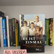 Im Hintergrund eine Reihe Bücher. Im Vordergrund das Buch"Es ist einmal. Ostdeutsche Großeltern und ihre Enkel im Gespräch" von Sabine Michel und Dörte Grimm, daneben ein Schild mit dem Hinweis "Aus unserem Buchshop".