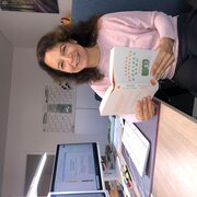 Unsere Kollegin Mirjam Deponte sitzt an ihrem Schreibtisch und hält ein Buch in der Hand.