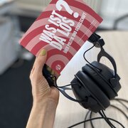 Eine Hand hält Kopfhörer und die Postkarte für den Podcast "Was ist da los? Über Politik und Gesellschaft".