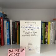 Im Hintergrund eine Reihe Bücher. Im Vordergrund das Buch „Die Unvereinigten Staaten. Das politische System der USA und die Zukunft der Demokratie“ von Stephan Bierling. 