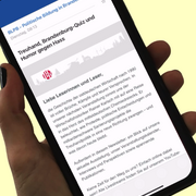 Eine Hand hält ein Smartphone. Auf dem Display läuft ein Video. Darin wird durch den Newsletter der Landeszentrale gescrollt. 