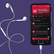 Ein Smartphone. Das Display zeigt den Podcast "Was ist da los? Über Politik und Gesellschaft" der Landeszentrale. Neben dem Smartphone liegen Kopfhörer.