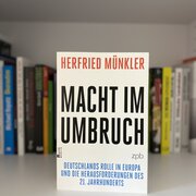 Im Hintergrund eine Reihe Bücher. Im Vordergrund das Buch „Macht im Umbruch“ von Herfried Münkler. 