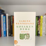 Im Hintergrund eine Reihe Bücher. Im Vordergrund das Buch "Kosakenberg" von Sabine Rennefanz.