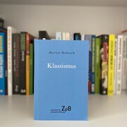 Im Hintergrund eine Reihe Bücher. Im Vordergrund das Buch "Klassismus" von Marlen Hobrack.