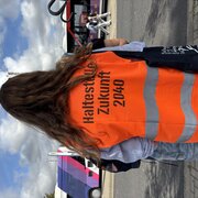 Eine Person in einer orangefarbenen Warnwest. Auf dem Rücken der Weste steht: Haltestelle der Zukunft 2040. 