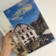 Eine Hand hält das Buch "Das Dorf" vor eine weiße Wand"