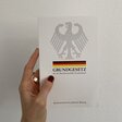 Eine Hand hält eine Ausgabe des Grundgesetz vor eine weiße Wand.