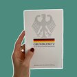 Eine Hand hält ein Grundgesetz hoch.