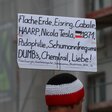 Ein Mann trägt ein Schild mit wirren Begriffen wie "Flache Erde, Eisring, Cabale, Schumannfrequenz..." etcorien