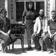 Vier Personen vor einem Gebäude - das Atelier der Gruppe "Clara Mosch" - mit den Schriftzügen 'CLARA' und 'MOSCH' auf Holztafeln.
