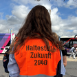Eine junge Frau trägt eine orangene Weste mit der Aufschrift "Haltestelle Zukunft"