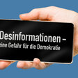Handy mit der Aufschrift Desinformationen - eine Gefahr für die Demokratie