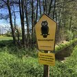 Foto mit einem gelben Schild für Naturschutz mit einer schwarzen Eule darauf